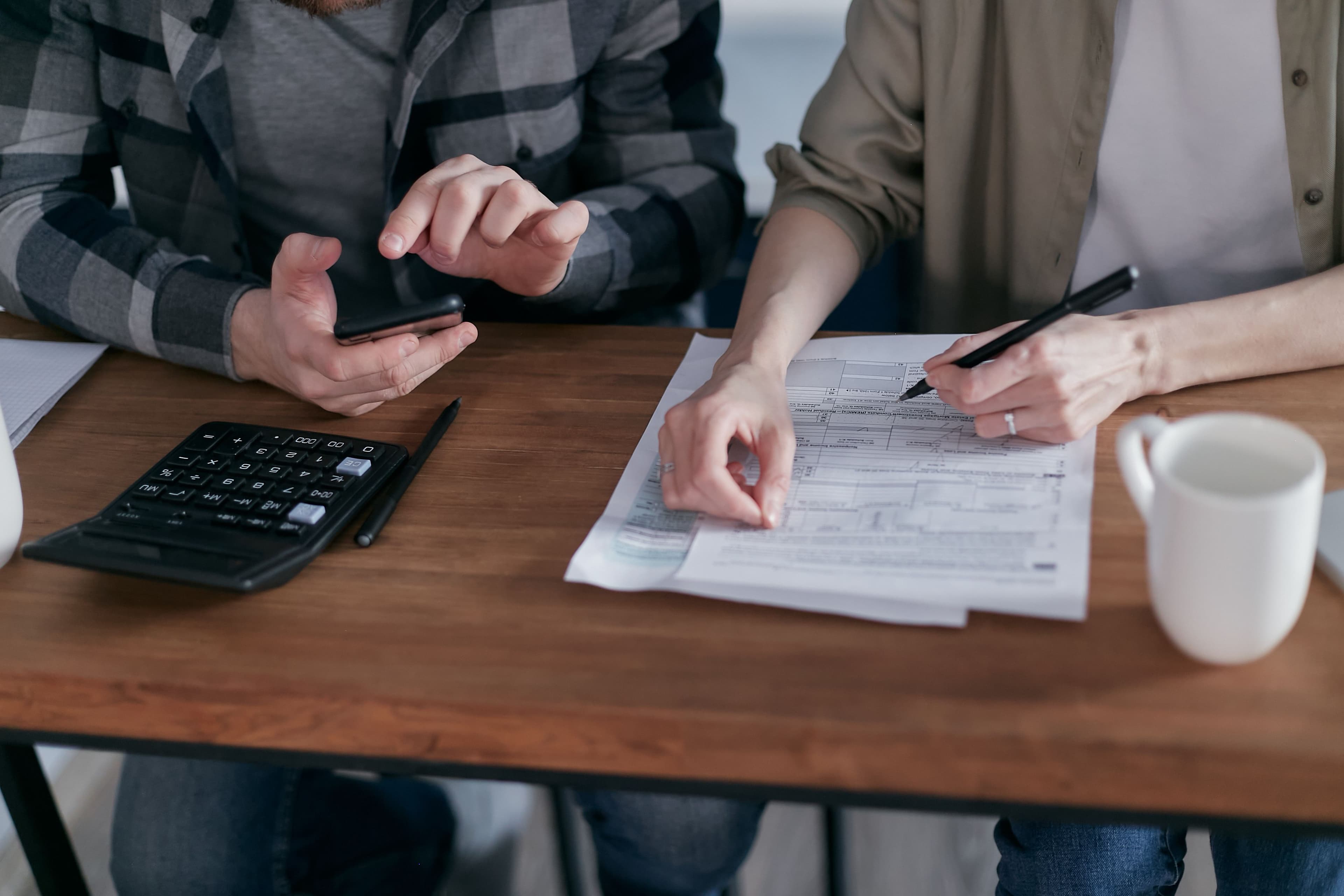 Hands reviewing a 1040 tax form on a desk, next to a calculator and a phone
